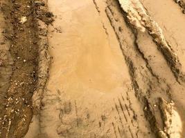 Textur einer schmutzigen, schlechten Schotterstraße Schotterstraße mit Pfützen und trocknendem Lehmschlamm mit Rissen und Furchen. Offroad. der Hintergrund foto