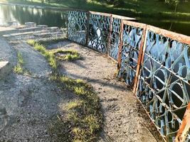 altes eisenblaues Metall rostiges Peelinggeländer, Zäune mit abblätternder rissiger Farbe vor dem Hintergrund des Wassers, des Flusses foto