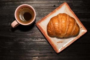 frühstückscroissant in teller und kaffee auf holztisch. foto