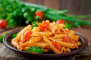 Penne-Nudeln in Tomatensauce mit Hähnchen und Tomaten auf einem Holztisch foto