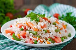 appetitlicher gesunder Reis mit Gemüse in weißer Platte auf einem hölzernen Hintergrund. foto