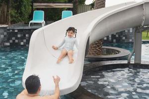 asiatischer vater und tochter schwimmen, spielen rutschenpool im pool des resorts, lächeln und lachen. spaß im pool des resorthotels, familienfreundliches konzept. foto