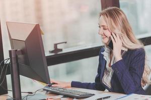 Geschäftsfrau, die im Büro mit geschäftlichem Telefonanruf arbeitet, während sie den Computer am Schreibtisch im Vintage-Farbton verwendet foto