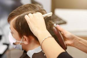 Ein Teenager in einem Schönheitssalon lässt sich die Haare schneiden, ein Friseur schneidet einem Teenager die Haare.