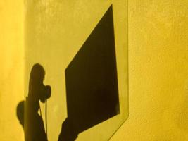 Fotografen beschatten einen Spiegel gegen die gelbe Wand foto