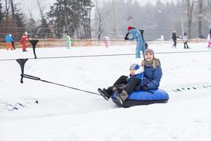 familie, die spaß auf der schneeröhre hat. mutter mit kind fährt einen schlauch. Menschen, die auf der Röhre bergab rutschen. Fahrstuhl fahren foto