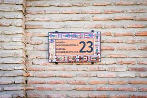 Backsteinmauer mit stilvoller Zierhausnummer und Straßennamenschild in der Altstadt von Telavi. bidzina cholokashvili straße historischer alter häuser. georgisches erbe in kachetien foto