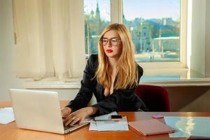 charmante blonde sekretärin im büro, die mit laptop und dokumenten arbeitet foto