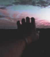 Hand streckt den Sonnenuntergang bei natürlichem schlechten Licht aus foto