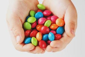 Mehrfarbige Bonbons in den Händen eines Kindes auf einem weißen, isolierten Hintergrund. geringer Kontrast foto