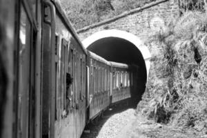 spielzeugeisenbahn, die sich am berghang bewegt, schöne aussicht, eine seite des berges, eine seite des tals, die auf der eisenbahn zum hügel fährt, inmitten grüner naturwälder. spielzeugeisenbahn von kalka nach shimla in indien-schwarz und weiß foto