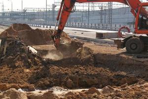 baggermaschinen, die auf der baustelle einer neuen straße in die stadt arbeiten. Orange Bagger gräbt Sand und Kies. Konzept der Renovierung von Gebäuden, Brücken und Straßen. Überbevölkerungsproblem. foto