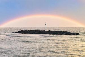 Steinbuhnen, Wellenbrecher im Wasser vor der Küste in Dänemark. Regenbogen foto