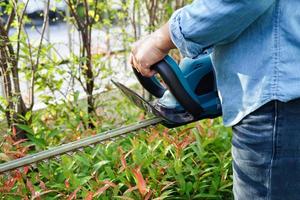 Gärtner trimmt Busch mit elektrischen Heckenscheren im Garten. Hobby zu Hause. foto