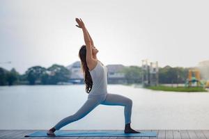 junge asiatische gesunde frau, die yoga im park am seepier macht. foto