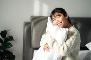 Lächelnde Frau, die zu Hause ein Kissen auf dem Bett umarmt foto