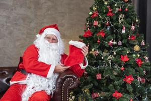 der weihnachtsmann hält eine weihnachtsgeschenkbox mit einem vollständig geschmückten chrsitmas-baum für die jahreszeitfeier und ein frohes neues ereigniskonzept foto