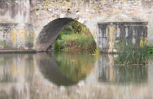 Nahaufnahme und Detailaufnahme des Bogens einer alten Steinbrücke. Die Brücke spiegelt sich im ruhigen Wasser eines Flusses. foto