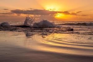 Ozeanwellen, die während des Sonnenuntergangs am Ufer abstürzen foto