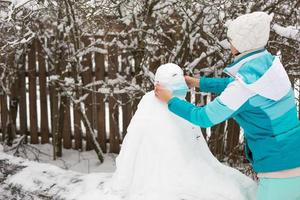 schneemann in einer medizinischen maske - eine neue realität, schutz vor krankheiten, infektionen, leben in der covid-epidemie. Frauenhände setzen eine Schneemannmaske auf. Outdoor-Aktivitäten für die Winterfamilie foto