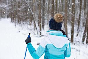 Skifahrer in Windjacke und Hut mit Bommel mit Skistöcken in den Händen mit dem Rücken vor dem Hintergrund eines verschneiten Waldes. Langlaufen im Winterwald, Sport im Freien, gesunder Lebensstil. foto