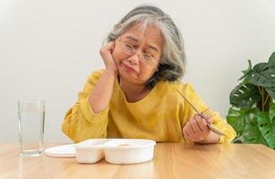 unglückliche asiatische seniorin anorexie und nein sagen zu fertiggerichten, allein zu hause alten menschen und gelangweiltem essen und appetitlosigkeit foto