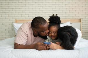 Die Familie hat Spaß und spielt Bildungsspiele online mit einem Smartphone zu Hause im Schlafzimmer. Konzept der Online-Bildung und Betreuung durch die Eltern. foto