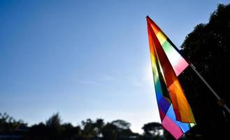 regenbogenfahne, die in der hand vor blauem hintergrund hält, konzept für die lgbt-feier im stolzmonat juni auf der ganzen welt. foto