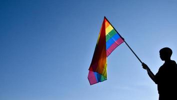 regenbogenfahne, die in der hand vor blauem hintergrund hält, konzept für die lgbt-feier im stolzmonat juni auf der ganzen welt. foto