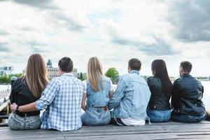 Gruppe von Menschen, die auf einem Pier neben einem Fluss sitzen foto