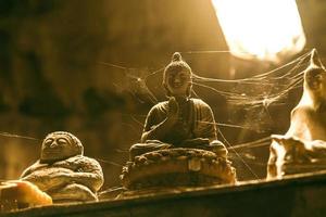 Nahaufnahme von steinernen Buddha-Statuen, die in einem Spinnennetz in einer Höhle bedeckt sind. foto