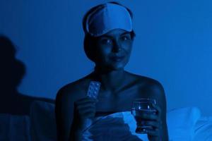 Frau im Schlafzimmer mit einem Glas Wasser und Schlaftabletten foto