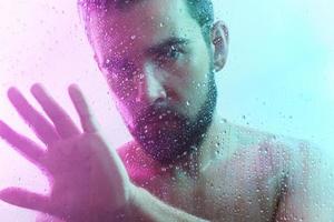 Porträt eines gutaussehenden Mannes durch nasses Glas im Neonlicht foto