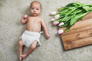 süßes kleines baby liegt neben dem blumenstrauß aus tulpen auf dem boden foto