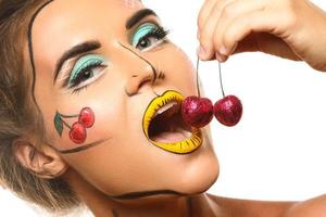 Schönes Modell mit kreativem Pop-Art-Make-up isst Kirschen foto