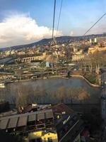 vertikaler blick von der seilbahn auf die schöne touristenstadt mit gebäuden und häusern, dächern mit bäumen und pflanzen, natur vor blauem himmel und bergen. europäische alte architektur foto