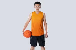 männlicher Basketballspieler, der Sportkleidung trägt, die Basketball auf weißem Hintergrund hält. foto