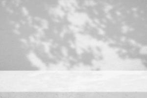 Weißer Grunge-Marmortisch mit Baumschatten auf Betonwand-Texturhintergrund, geeignet für Produktpräsentationshintergrund, Display und Attrappe. foto