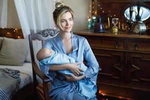 junge schöne mutter mit ihrem niedlichen kleinen baby, das in das blaue tuch gehüllt ist foto
