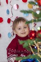 ein kind am weihnachtsbaum mit girlanden legt geschenke darunter. die Emotionen der Kinder. weihnachten und neujahr. foto
