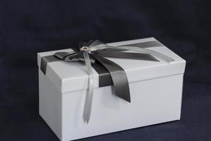 die geschenkbox ist weiß mit einer schönen grauen schleife. Geschenk auf dunklem Hintergrund. Feiertage und Überraschungen. Satinschleifen mit Strasssteinen. foto