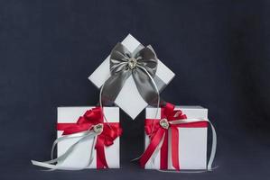 viele Geschenke. die geschenkbox ist weiß mit einer roten und grauen schönen schleife. Geschenk auf dunklem Hintergrund. Feiertage und Überraschungen. Satinschleifen mit Strasssteinen. foto