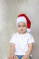 Porträt eines süßen kleinen Jungen in einem weißen T-Shirt und einem Weihnachtsmann-Hut. die Emotionen der Kinder. weihnachten und neujahr. erfolg, gute idee, kreative ideen und konzepte. foto