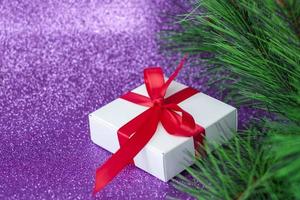 weißes Weihnachtsgeschenk mit roter Schleife. Geschenk unter dem Weihnachtsbaum auf lila Hintergrund. foto