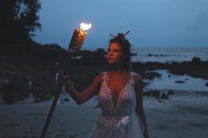 braut im schönen hochzeitskleid hält fackellicht am strand foto