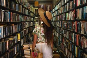 Schönes Mädchen mit stylischem Outfit auf der Suche nach einem interessanten Buch in der Vintage-Buchhandlung foto