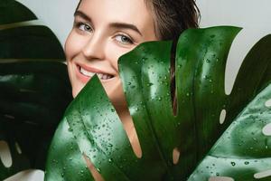 junge frau mit glatter haut, die monstera deliciosa pflanzenblatt hält foto