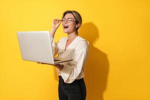 Fröhliche Frau mit Brille benutzt Laptop-Computer auf gelbem Hintergrund foto