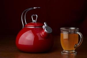 Ein roter Wasserkocher auf dunklem Hintergrund mit einer Tasse Tee foto