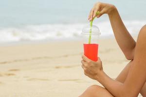 Frau mit einem roten Erfrischungsgetränk am Strand foto